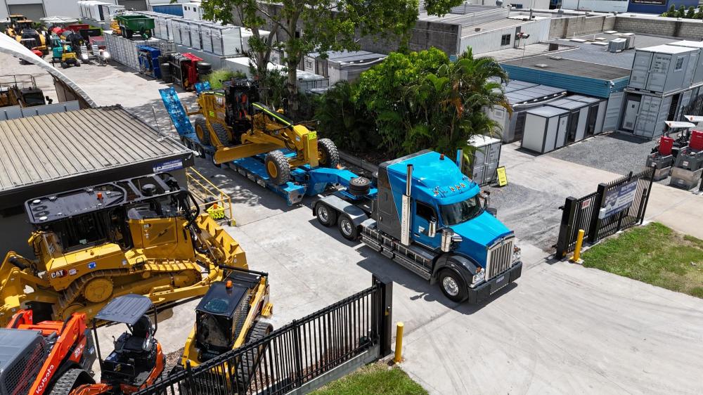 A blue truck with a yellow machinery on the trailer
